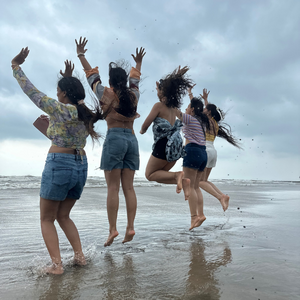 Women from the FinEdge team jumping joyfully on a beach with waves.