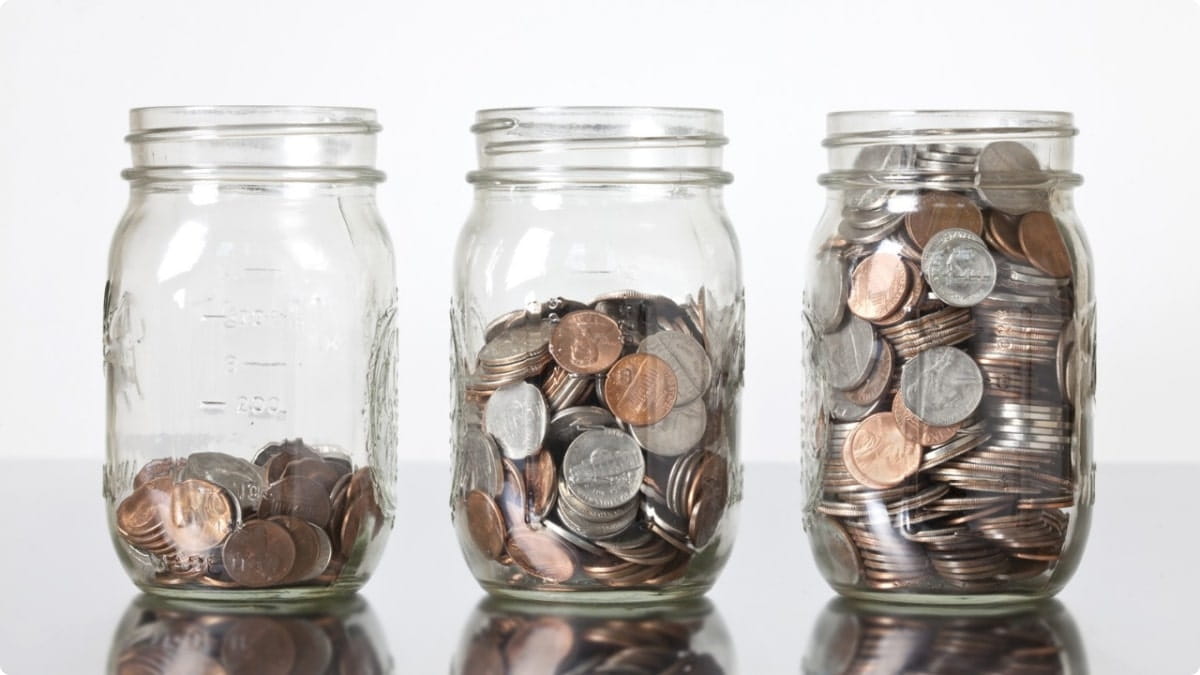 Three glass jars filled with increasing amounts of coins, illustrating year-end savings growth and the importance of reviewing and planning finances for long-term goals.